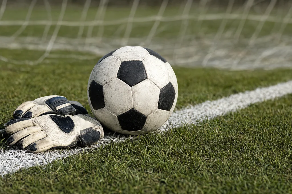 Goalkeeper gloves lying on the goal line beside a ball inside the six-yard box
